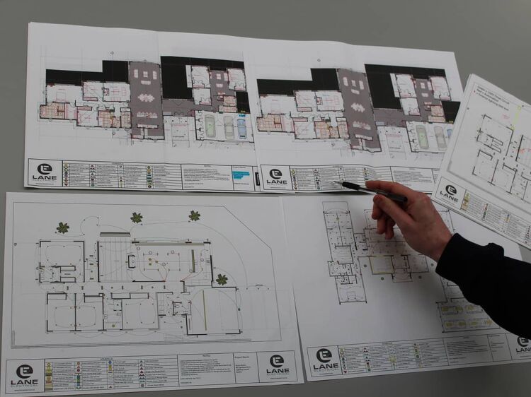 Electrical plans laid out on a table, hand pointing with a pen.